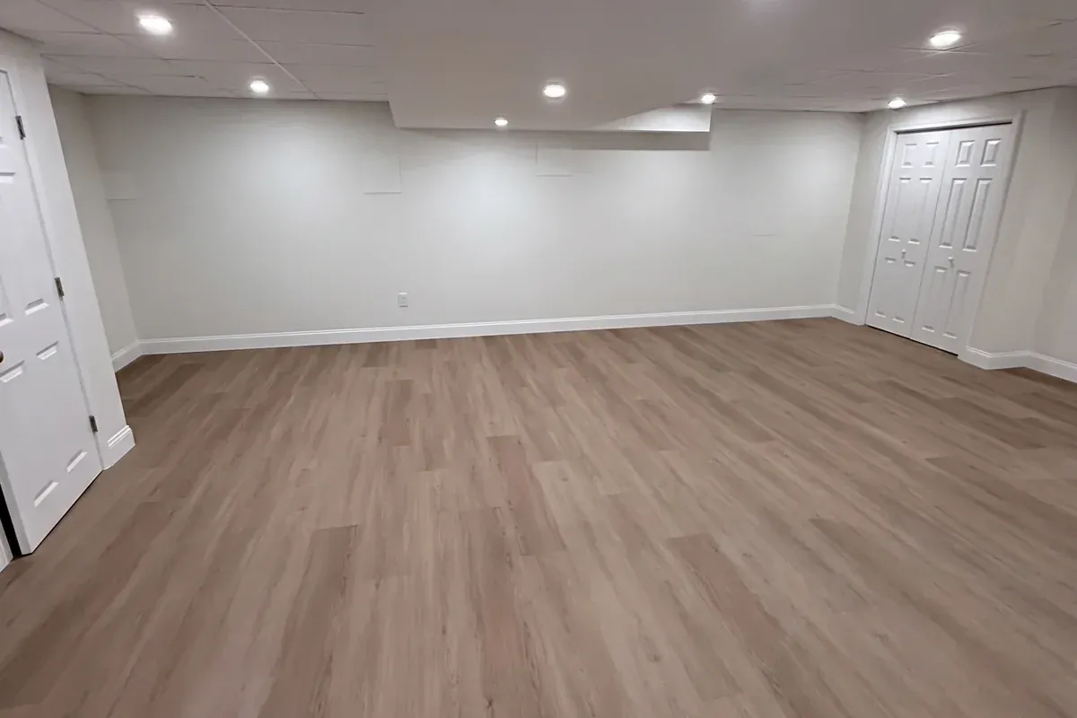 Wide view of a finished lower level with drop ceiling and wood-look vinyl floor, Innov Builders project in Chelmsford, MA