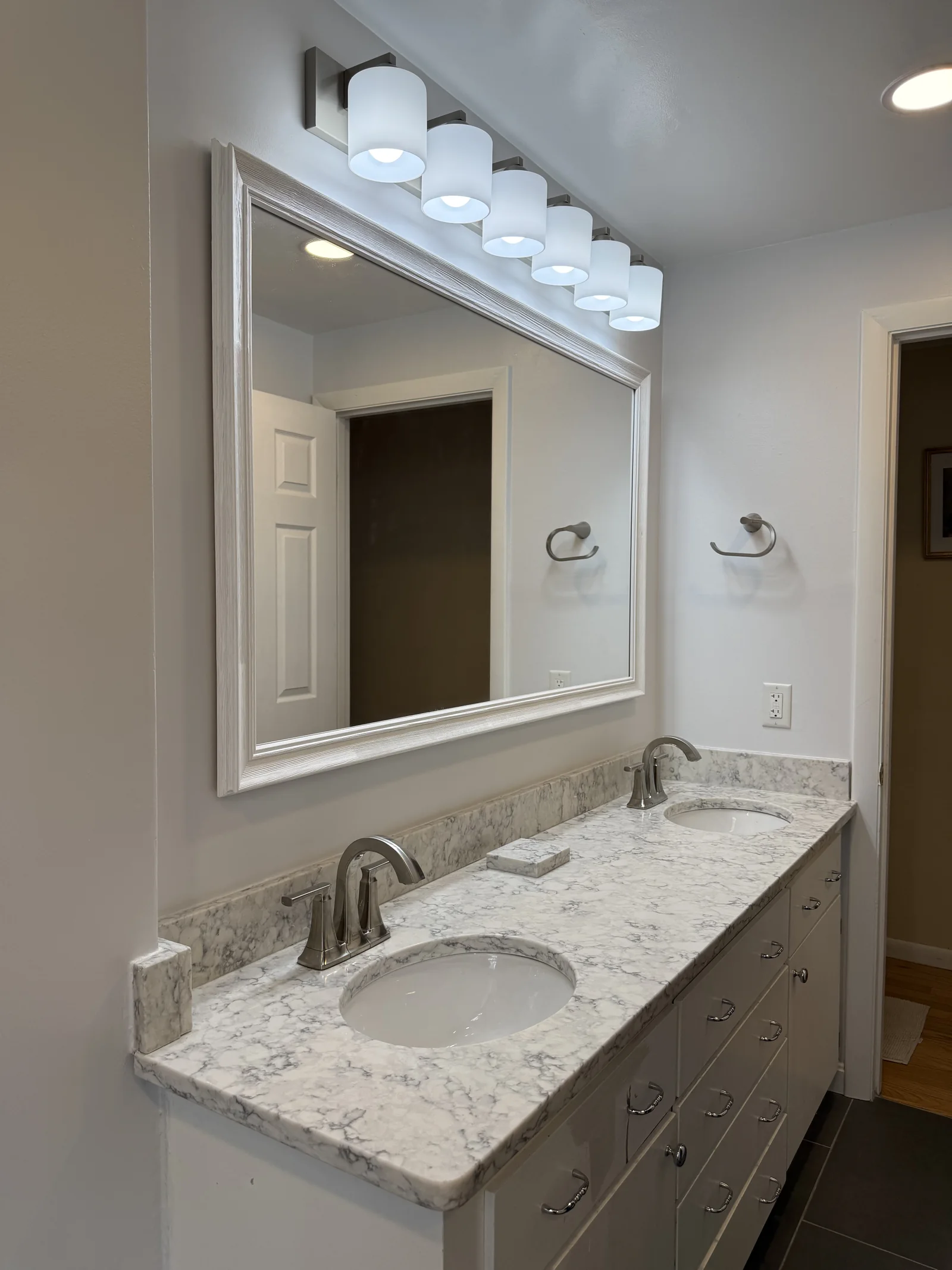 Double vanity bathroom remodel with marble countertop, white cabinetry, large mirror, and bright lighting in Wakefield MA